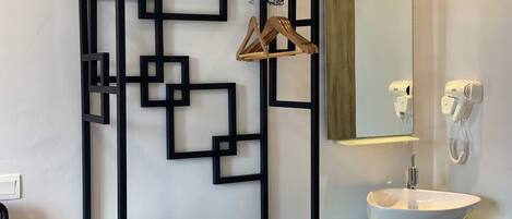 Un baño con un diseño geométrico en la pared de color negro, un lavamanos blanco, un espejo y un secador de pelo en la pared.
