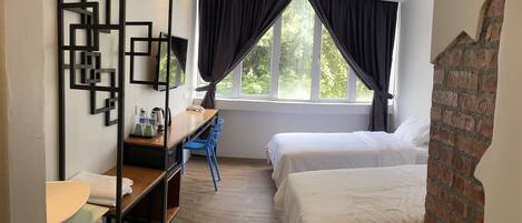 Habitación de hotel con escritorio de madera, dos camas, ventana con cortinas y pared de ladrillo.