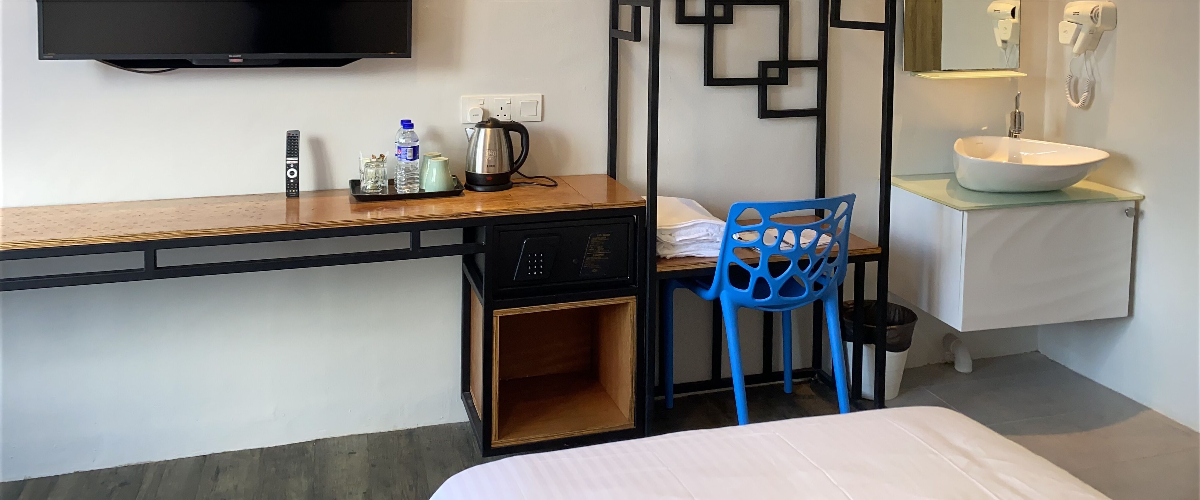 A hotel room with a wooden desk, a blue chair, a bed, a sink, and a television mounted on the wall.