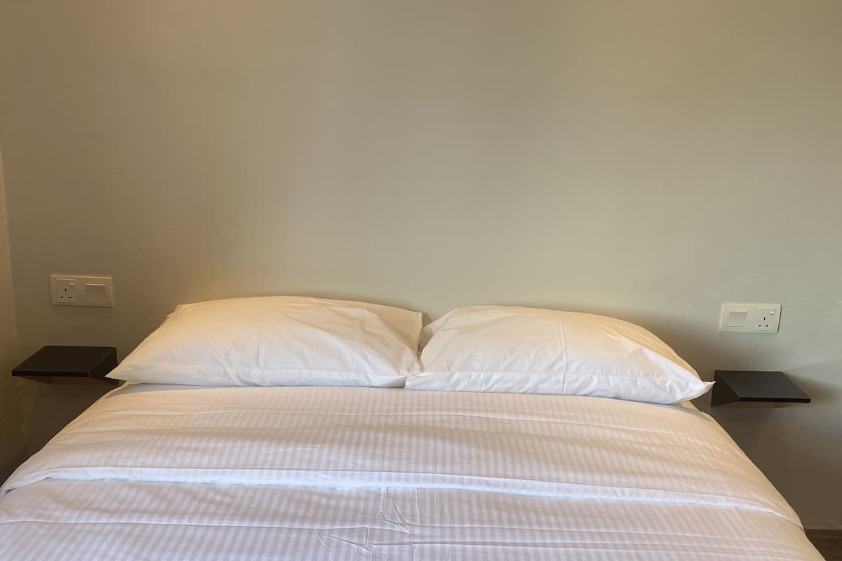 A bed with white bedding, two bedside tables, and a plain wall with electrical outlets.