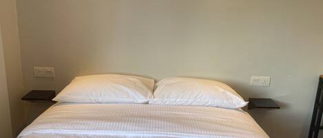 A bed with white bedding, two bedside tables, and a plain wall with electrical outlets.