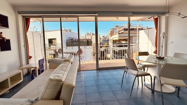 Amplia sala de estar con un gran ventanal corredero que da a un balcón, un sofá, una mesa de comedor con sillas y un televisor montado en la pared.