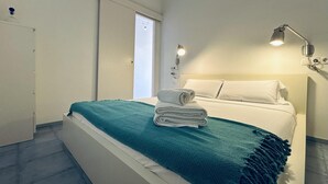 Un dormitorio moderno con cama, una manta color turquesa y almohadas blancas.