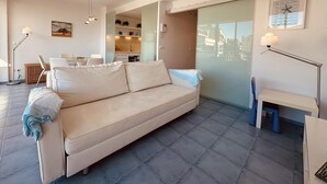 Una sala moderna con un sofá, una mesa de comedor y una cocina visible a través de una puerta abierta.
