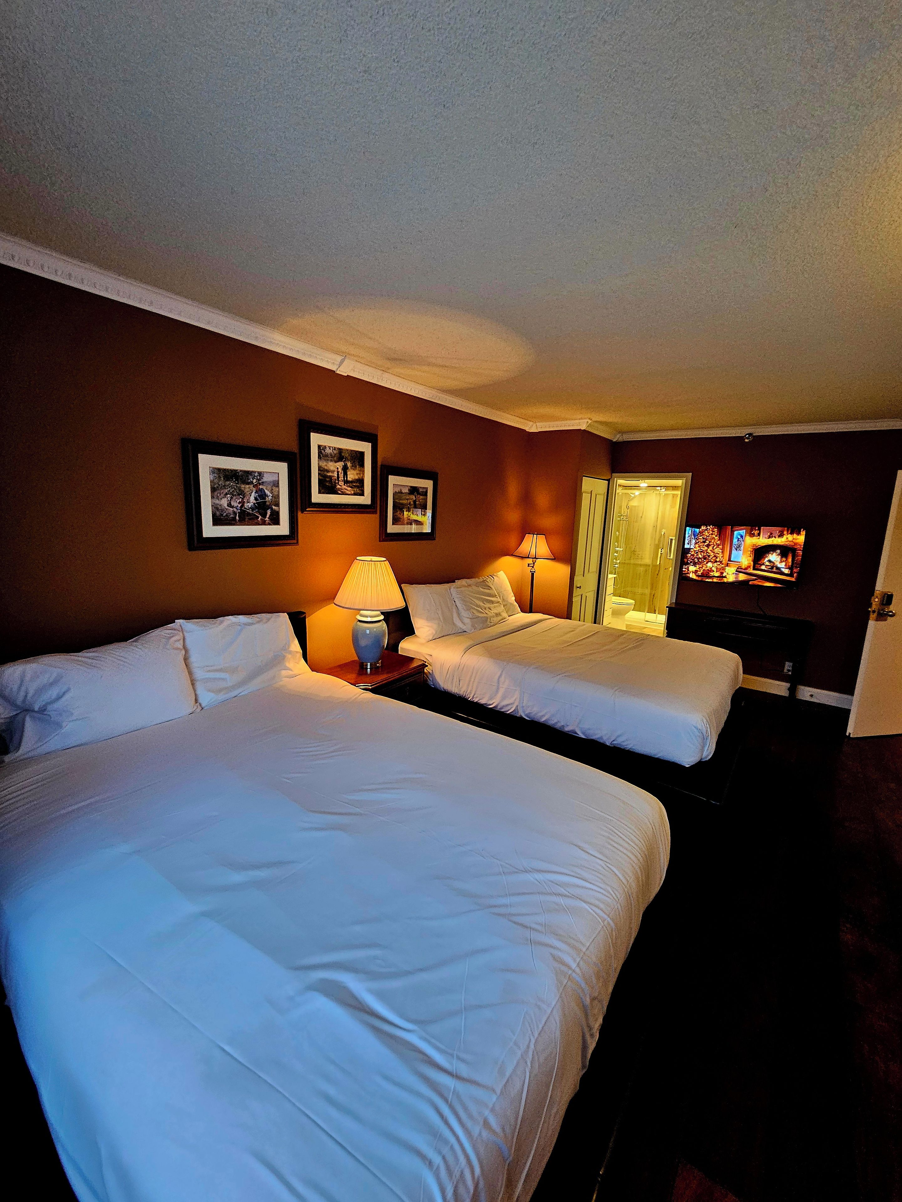A hotel room with two beds, a television, and framed pictures on the wall.