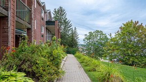 A brick pathway leading to a building with balconies, surrounded by lush greenery and trees. - Chambre 2 Lits/Room 2 beds (Saint-sauveur)