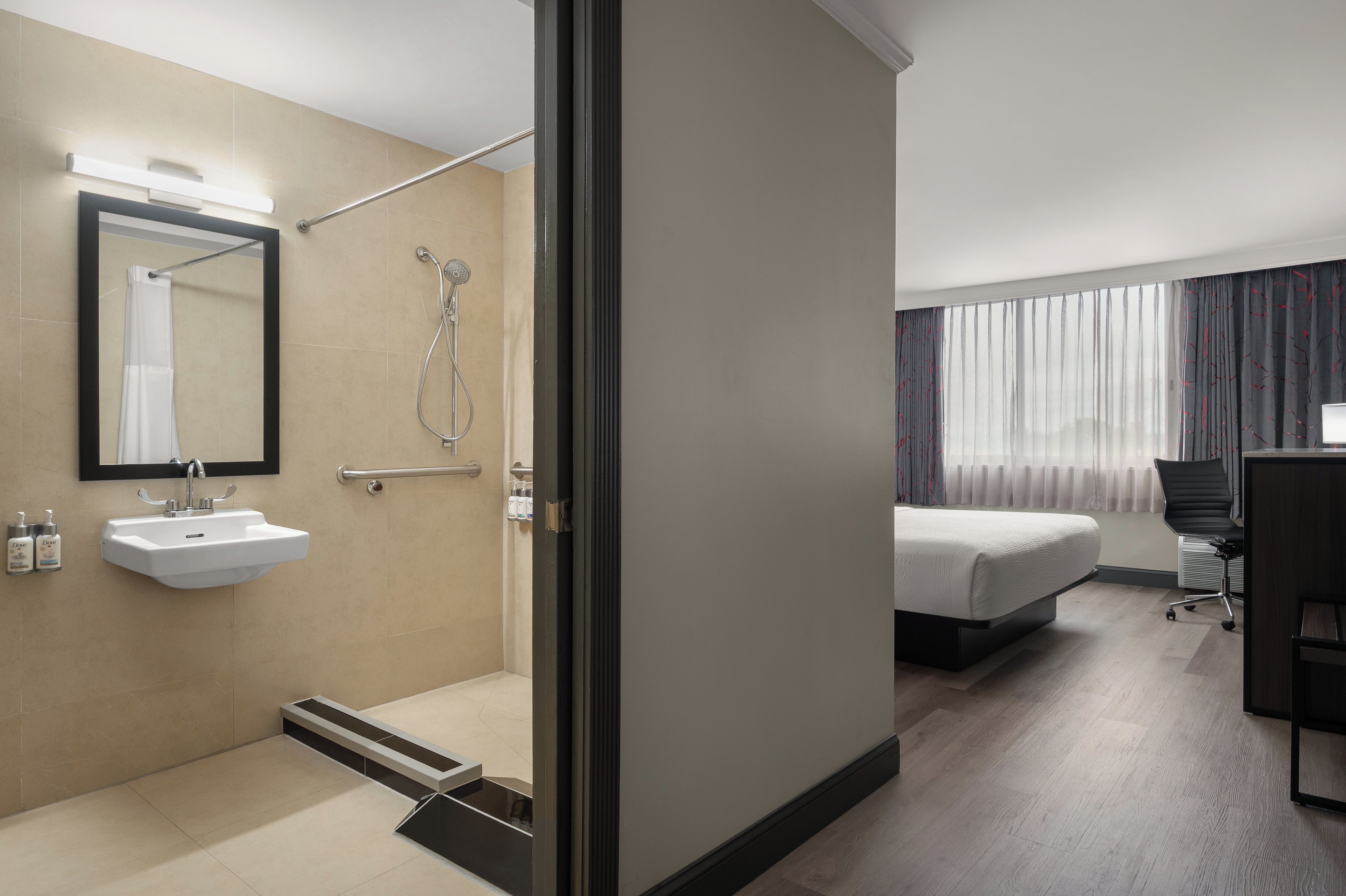 Ett hotellrum med badrum, säng, skrivbord och ett fönster med gardiner.