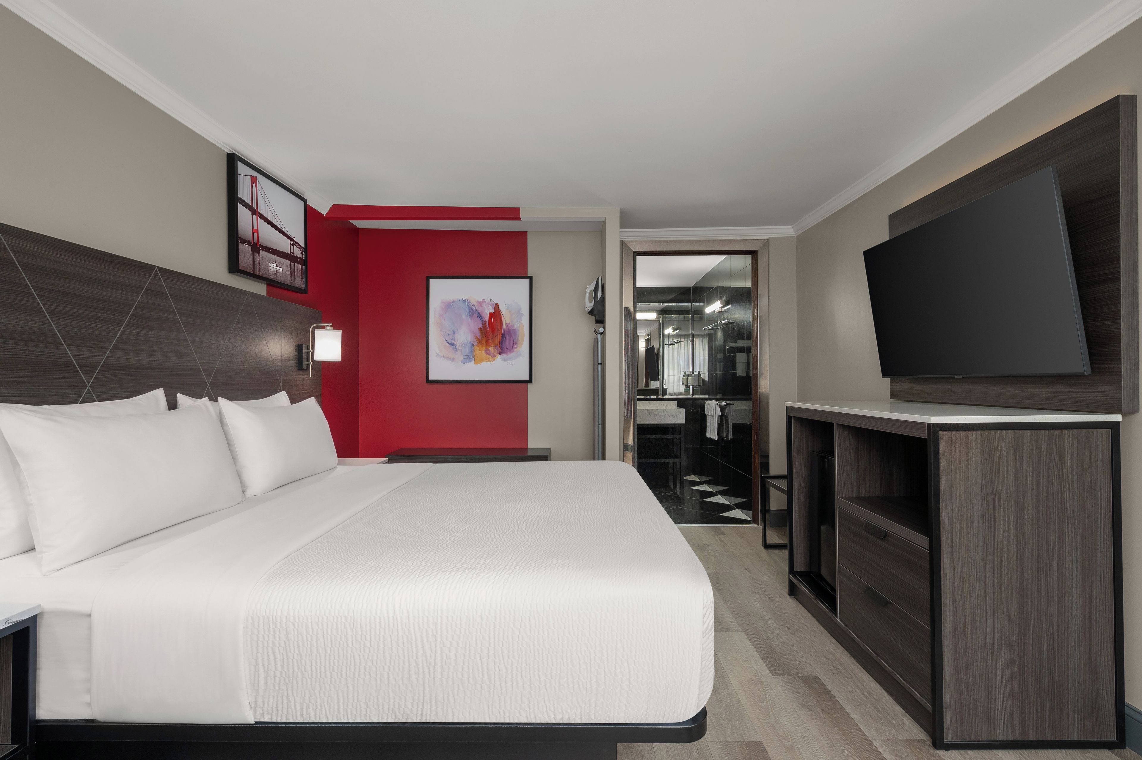 Ein Hotelzimmer mit einem großen Bett, einem Fernseher, einem Badezimmer mit Spiegel und einer roten Akzentwand.