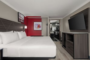 A hotel room with a large bed, a television, a bathroom with a mirror, and a red accent wall.