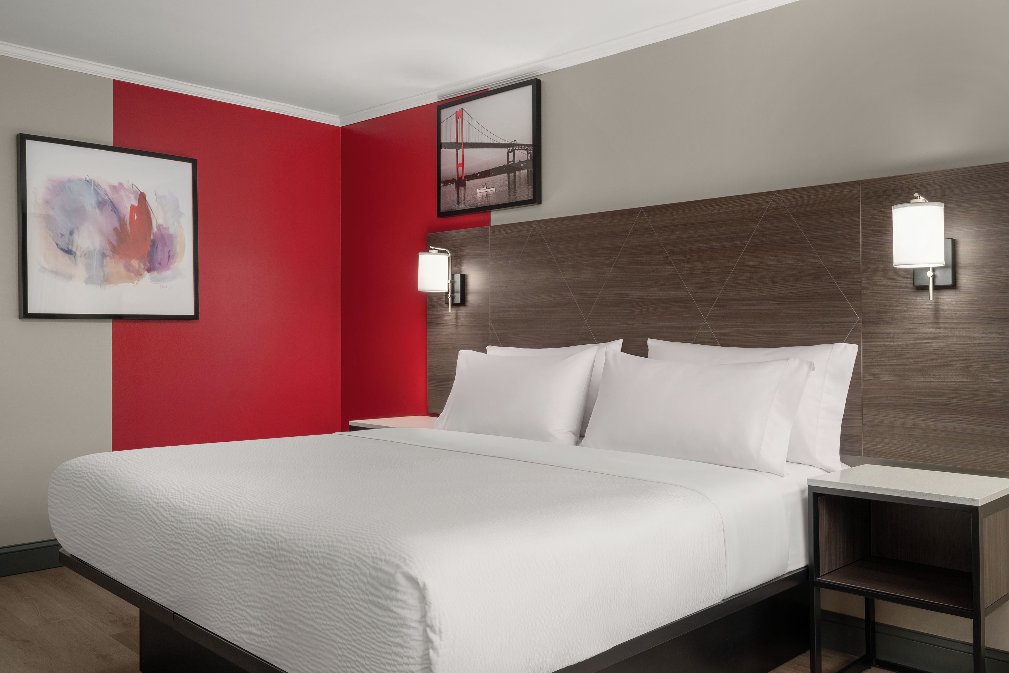 Une chambre d’hôtel avec un lit, une table de chevet, un mur d’accent rouge et deux lampes fixées au mur.