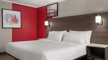 Een hotelkamer met een bed, nachtkastje, rode accentmuur en twee wandlampen.