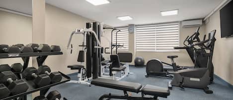 Une salle de sport équipée de divers appareils d’exercice, notamment des haltères, un banc et des appareils de cardio.