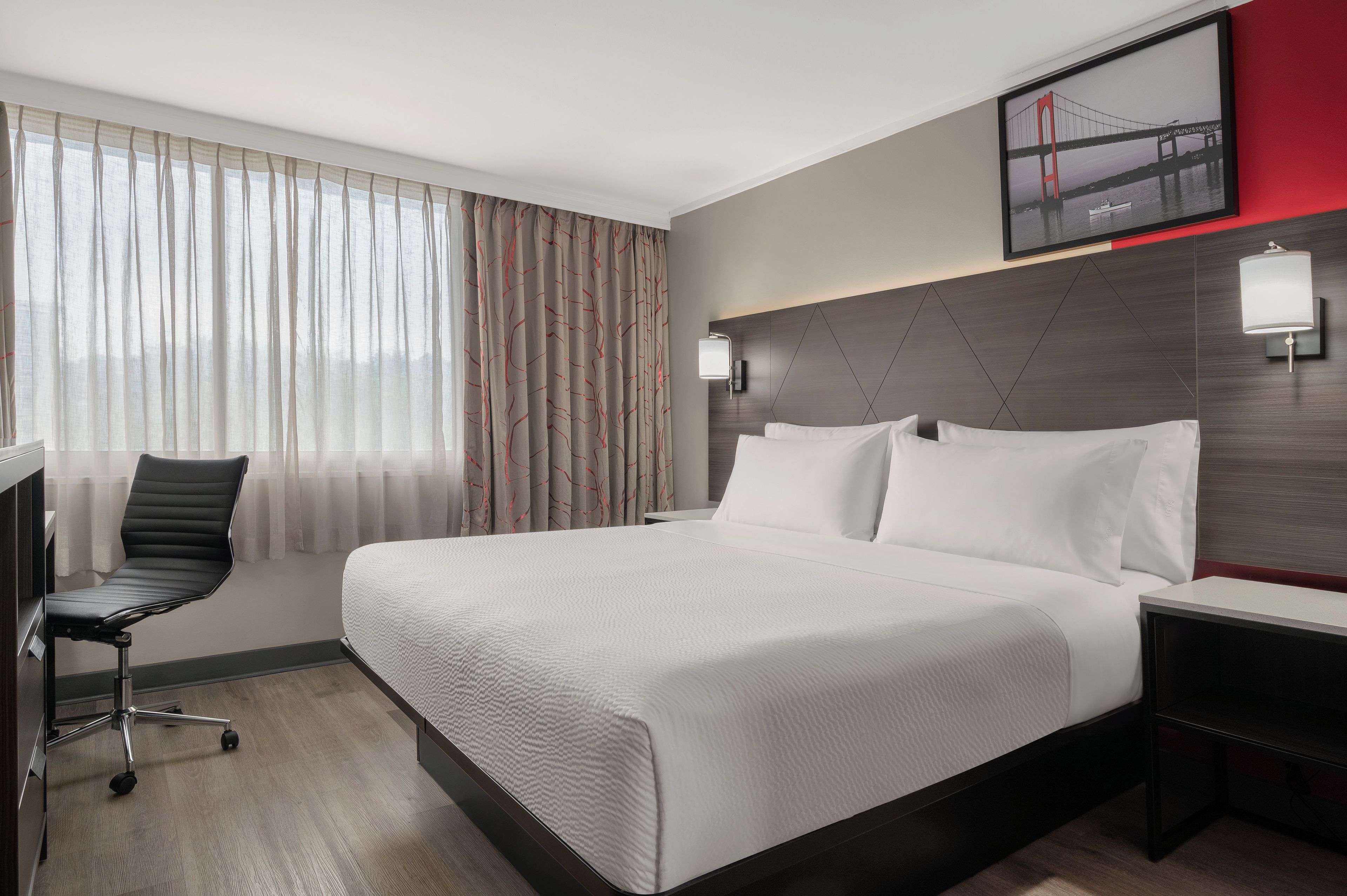 Ein Hotelzimmer mit einem Bett, einem Schreibtisch, einem Sessel und einem an der Wand befestigten Fernseher.