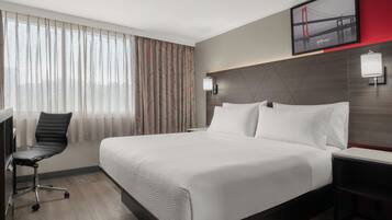 Ein Hotelzimmer mit einem Bett, einem Schreibtisch, einem Sessel und einem an der Wand befestigten Fernseher.