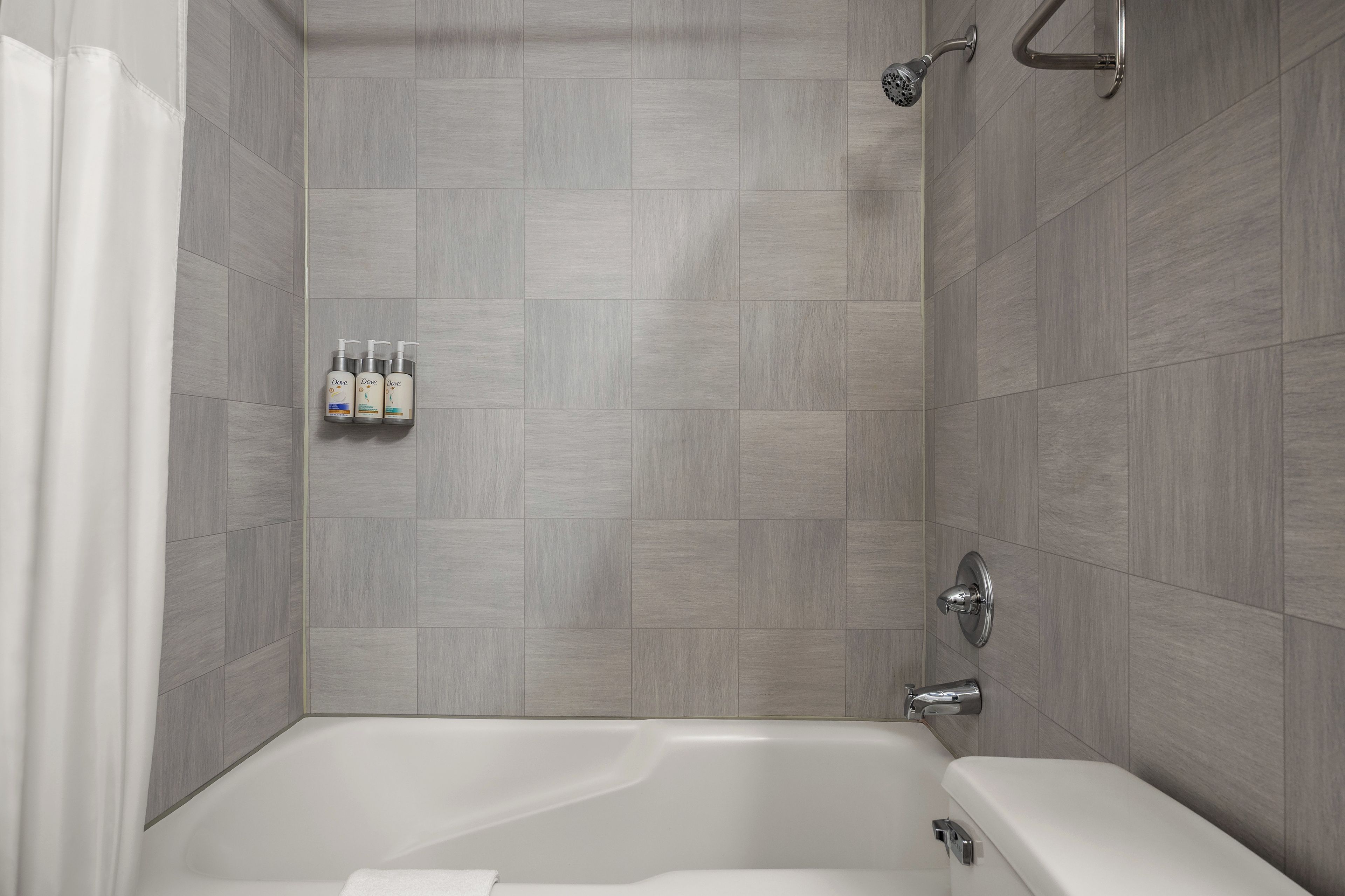 A modern bathroom with a bathtub, shower, and a set of Dove shampoo bottles on the wall.