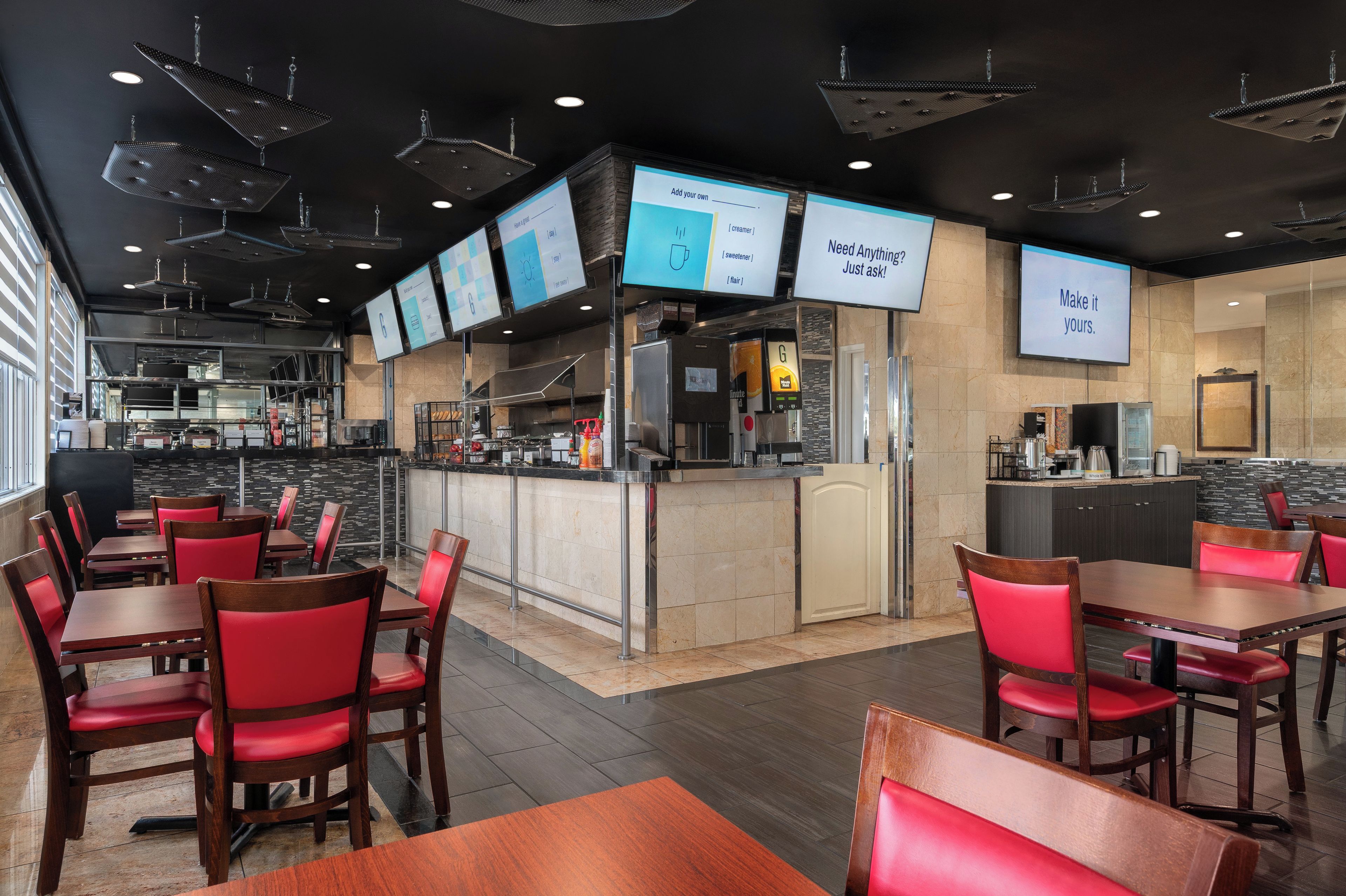 A modern restaurant interior with a bar area, multiple seating options, and digital menu displays.