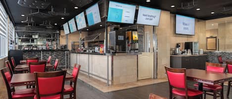 Un restaurante moderno con zona de bar, diversas opciones de asientos y pantallas digitales con el menú.