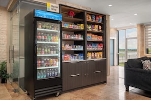 Una estación de bebidas de autoservicio con una variedad de bebidas y aperitivos, como agua embotellada, refrescos y papas fritas.