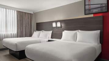 A hotel room with two beds, a headboard with wall-mounted lights, a window with sheer curtains, and a framed picture of a bridge.