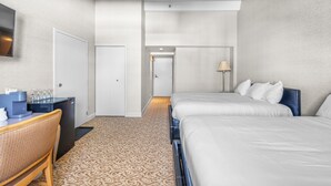 Une chambre d’hôtel avec deux lits, un bureau doté d’une machine à café, un téléviseur fixé au mur et une moquette à motifs.