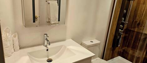 Un baño con un lavamanos blanco, un espejo, un inodoro y una zona de ducha.