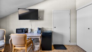 Une petite pièce compacte dotée d’une kitchenette, d’un téléviseur à écran plat, d’une porte blanche et d’un tapis à motifs.