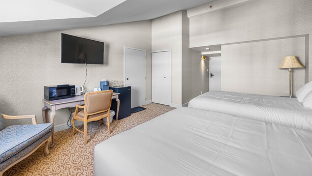 Une chambre d’hôtel équipée d’un lit, d’un bureau avec un ordinateur, d’une chaise, d’une télévision et d’une lampe.