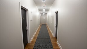 Un couloir étroit au sol en bois, aux murs blancs, et un paillasson noir à motifs qui mène à une porte portant le numéro 4.