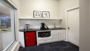Une cuisine compacte avec un réfrigérateur rouge, une machine à café et un four à micro-ondes. Deux tableaux encadrés sont accrochés au mur, au-dessus du plan de travail.