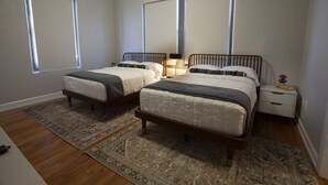 A bedroom with two beds, a nightstand, and a window. - Greyhound Inn - Classic Double Suite (Tyler)