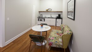 Une cuisine compacte équipée d’un four à micro-ondes, d’un grille-pain et d’un évier. Une petite table à manger avec une chaise se trouve au premier plan.