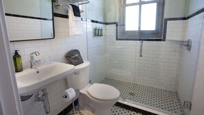 A bathroom with a white sink, toilet, and shower. There is a towel rack above the sink and a window above the shower. - Greyhound Inn - Deluxe King Suite (Tyler)