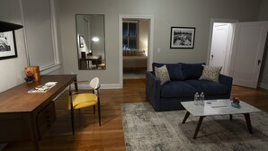 A living room with a wooden desk, a blue sofa, and a coffee table. - Greyhound Inn - Deluxe King Suite (Tyler)