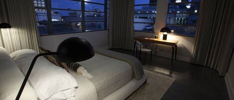 Un dormitorio con cama, escritorio y vista a la ciudad de noche.