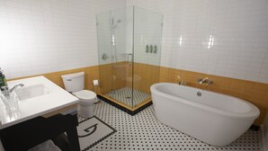 A bathroom with a glass-enclosed shower, a white bathtub, a toilet, and a sink. - Greyhound Inn - Deluxe King Suite (Tyler)