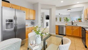A modern kitchen with stainless steel appliances, wooden cabinets, and a glass dining table with white chairs. - SWSS 3BR Kierland Greens Condo | Pool, Hot Tub, Golf Access & Gated Community (Scottsdale)