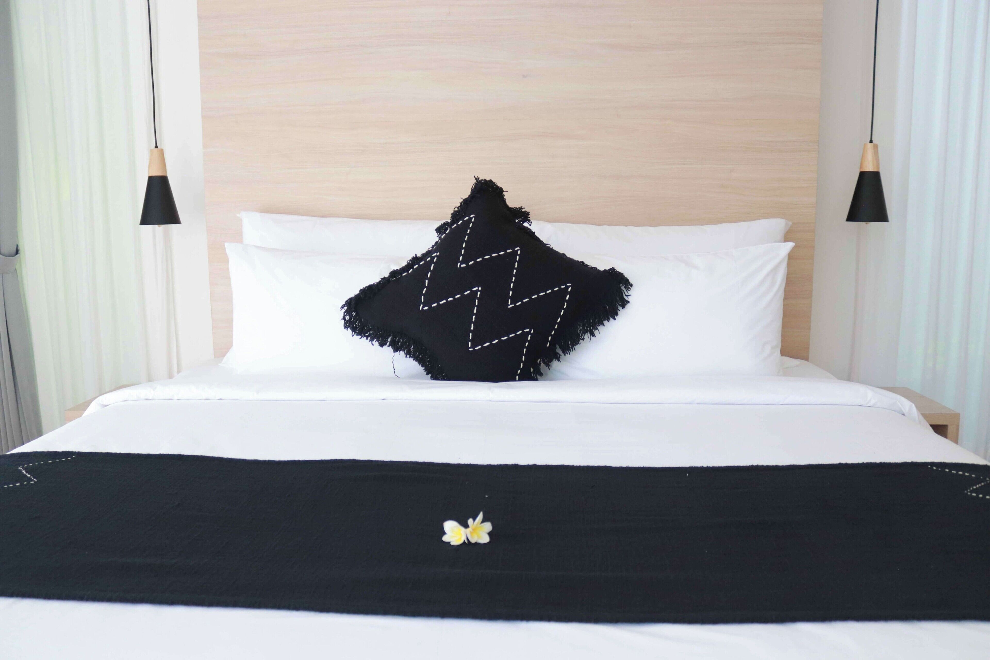 A bed with white bedding, a black zigzag pillow, and a black bedspread with a small yellow flower.