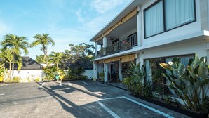 A modern two-story building with a paved courtyard, large windows, and tropical plants.