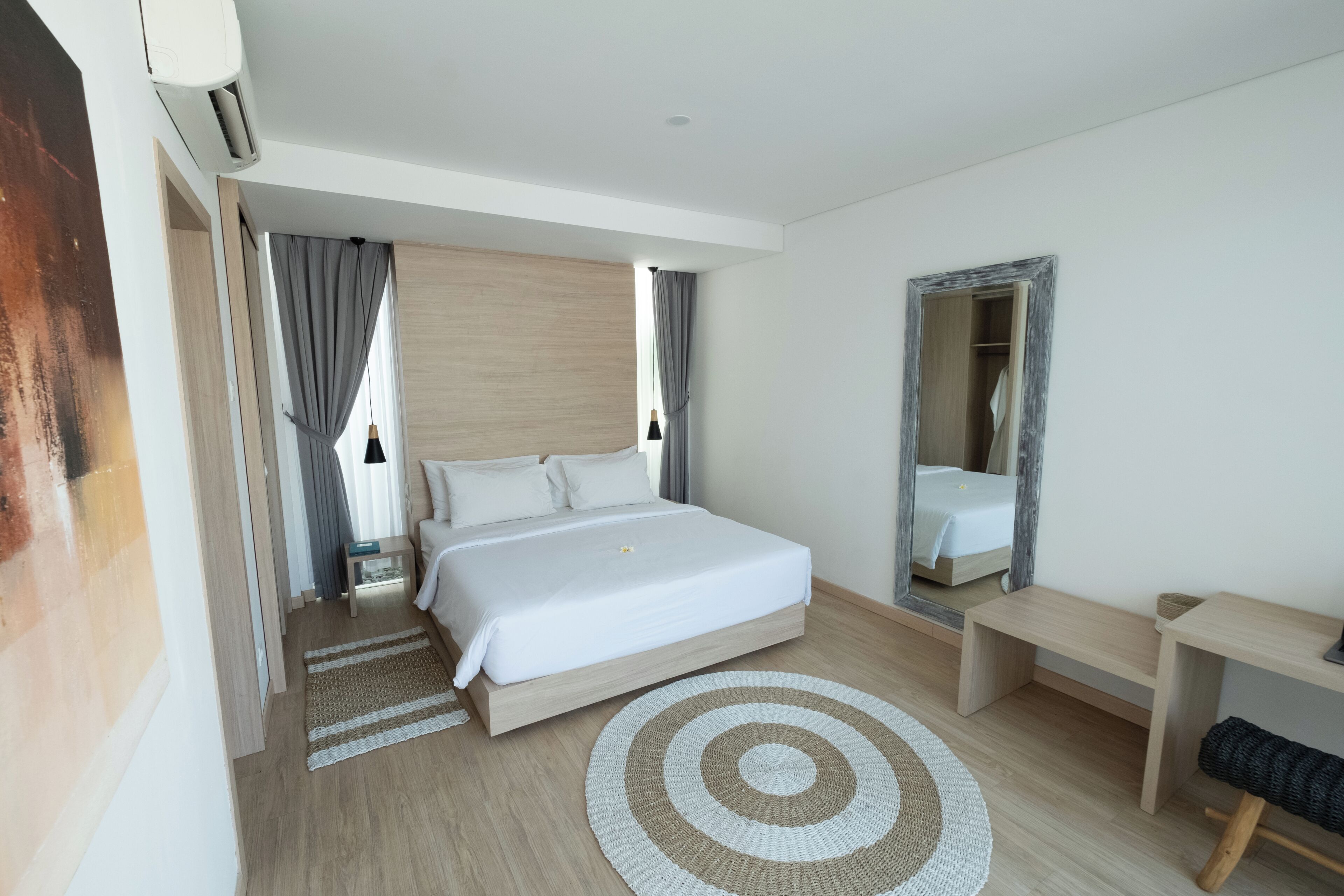 A modern hotel room with a large bed, bedside tables, a mirror, and a wooden floor.