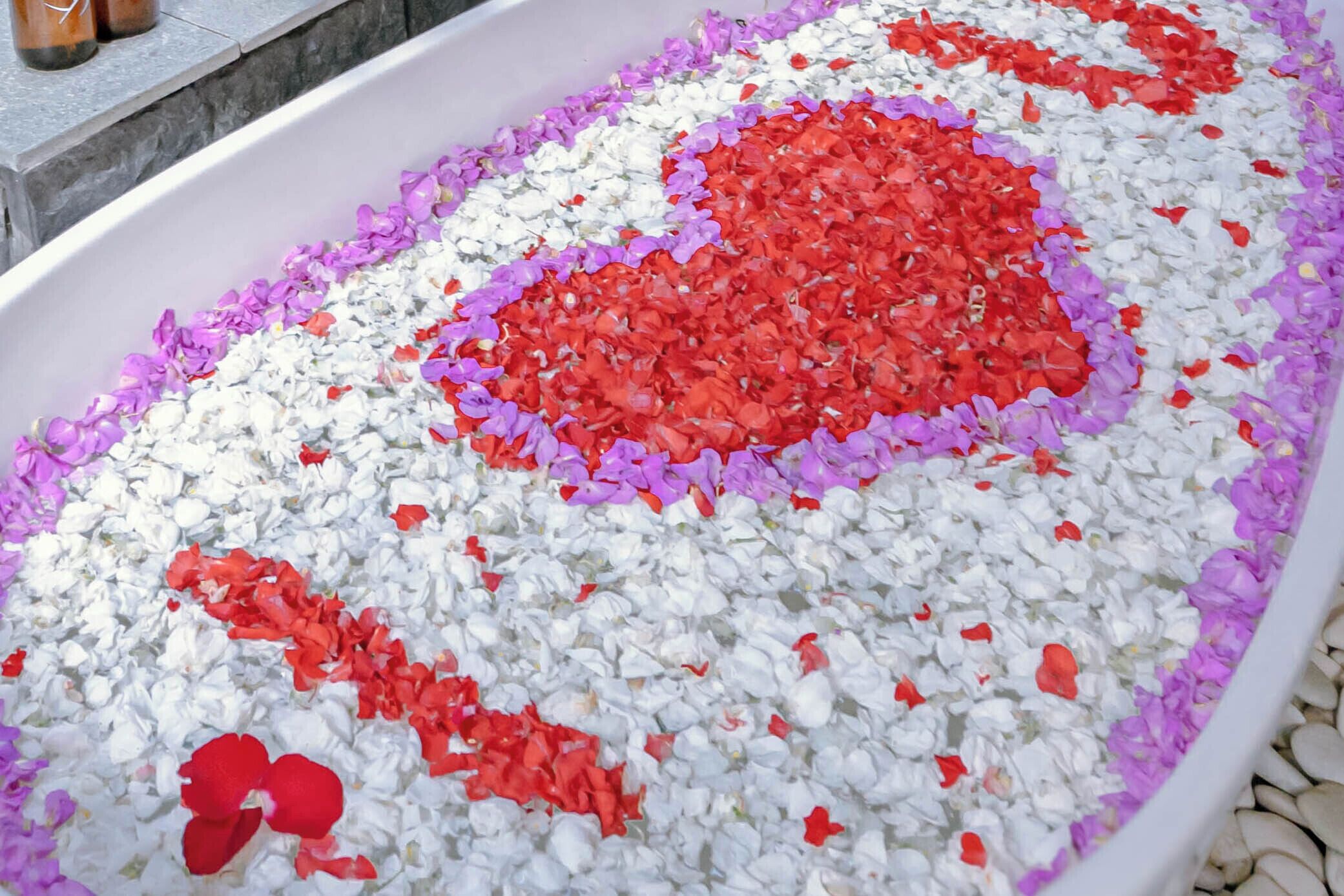 Une baignoire remplie de pétales de fleurs blanches et rouges disposées en forme de cœur.