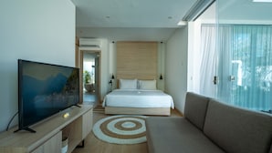 A modern hotel room with a large bed, a TV on a wooden stand, a sofa, and a view of the outdoors.