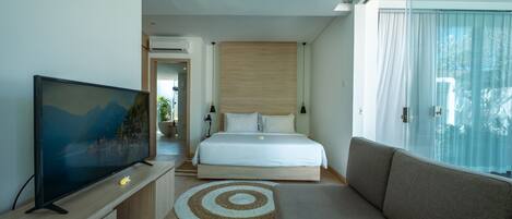 A modern hotel room with a large bed, a TV on a wooden stand, a sofa, and a view of the outdoors.