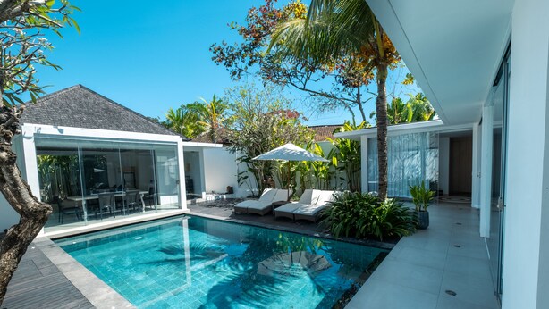 A modern pool area with a glass-enclosed patio, lounge chairs, and tropical plants.