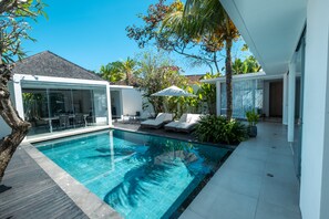 A modern pool area with a glass-enclosed patio, lounge chairs, and tropical plants.