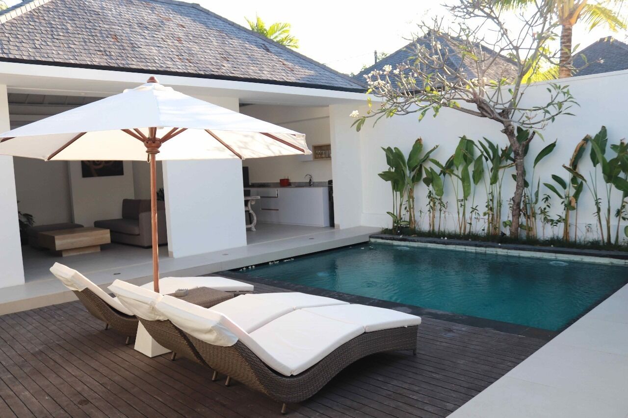 A poolside area with lounge chairs and a canopy, a small kitchen, and a white wall with plants.