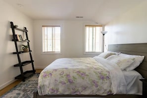A bedroom with a bed, a nightstand, a bookshelf, and two windows.