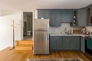 A modern kitchen with grey cabinets, a stainless steel refrigerator, and wooden flooring.