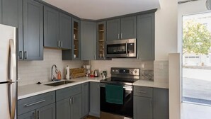 Une cuisine moderne avec des meubles gris, des appareils en acier inoxydable et un plan de travail blanc.