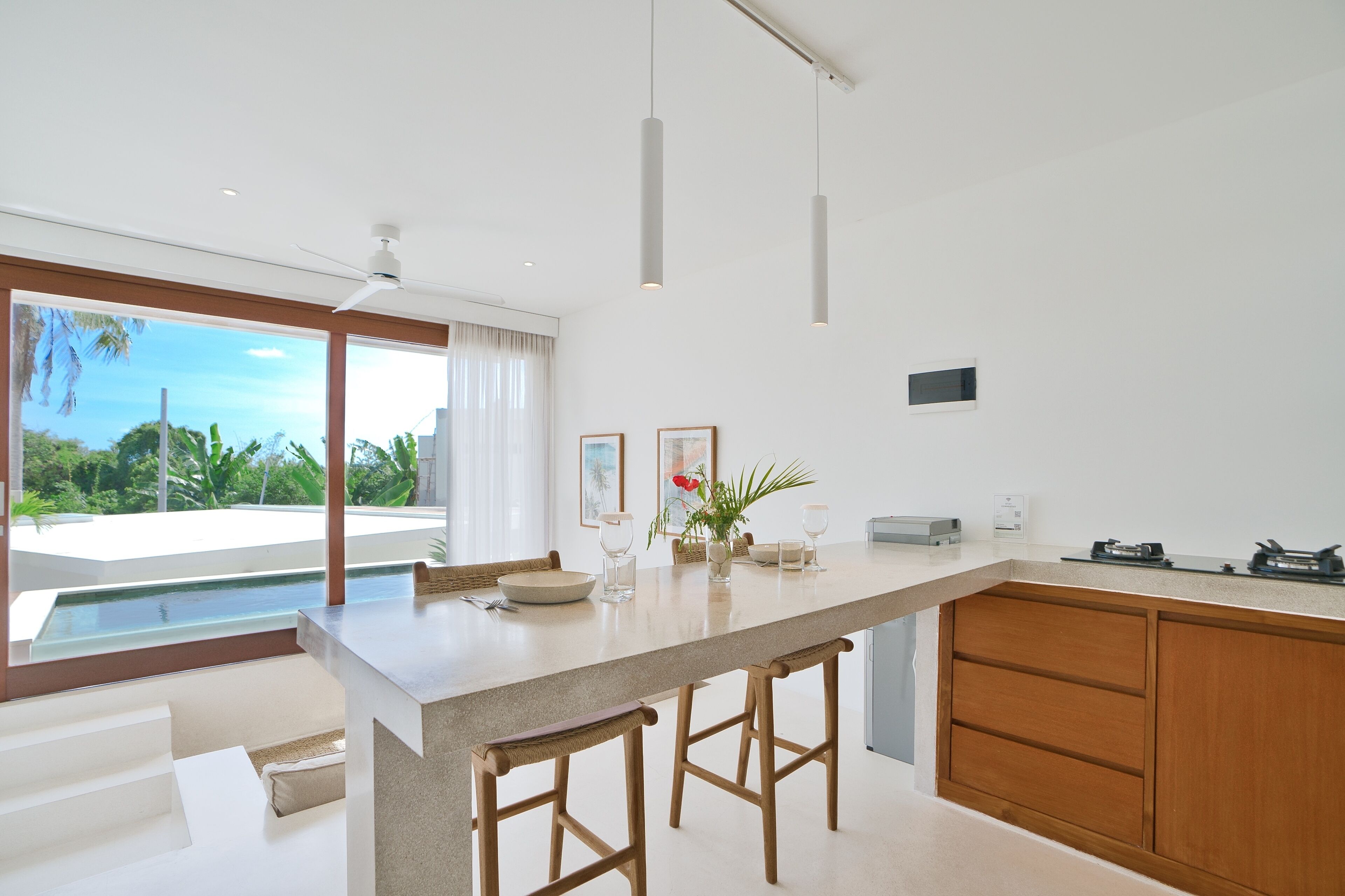 A modern kitchen with a large island, wooden stools, and a view of a pool and greenery.