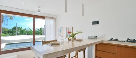 A modern kitchen with a large island, wooden stools, and a view of a pool and greenery.